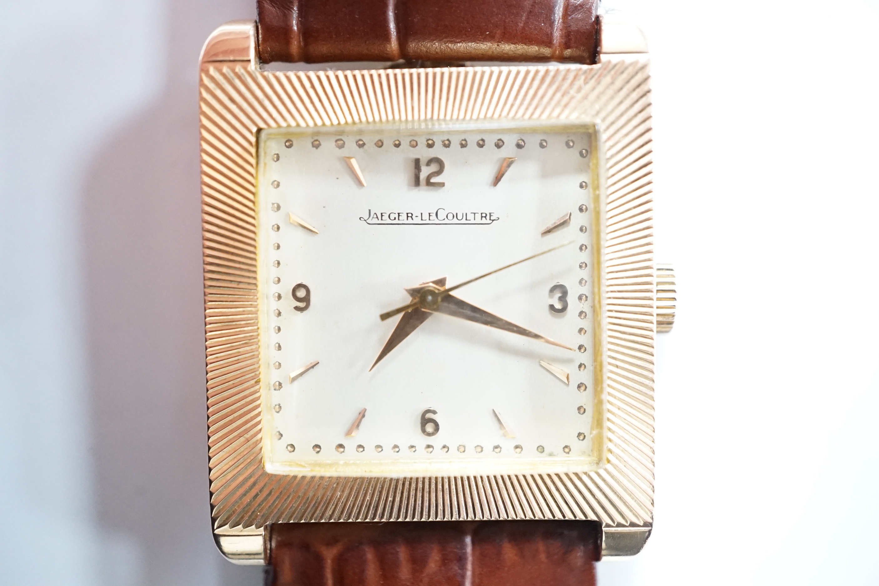 A gentleman's 18ct gold Jaeger LeCoultre manual wind dress wrist watch, with square dial, milled bezel and baton and quarterly Arabic numerals, on associated leather strap, case diameter 26mm, gross weight 31.8 grams.